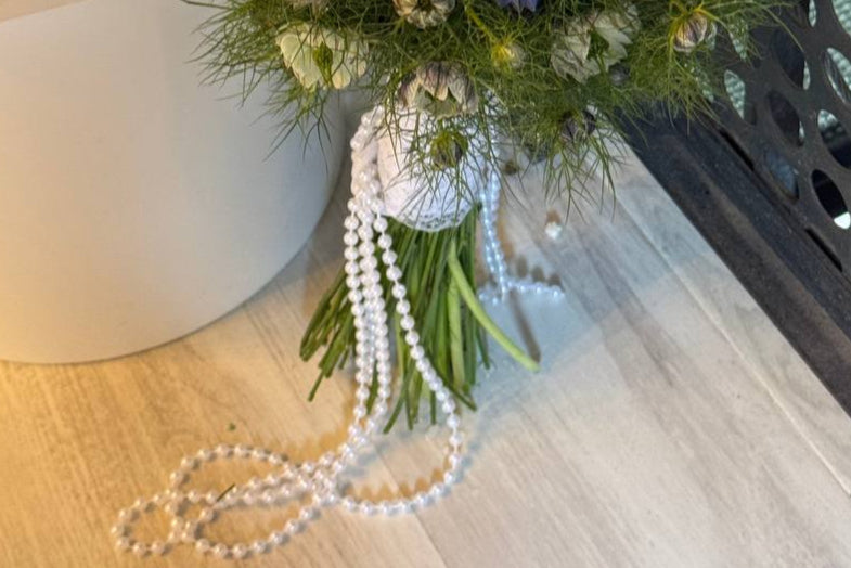 Pearl necklace draped over a bouquet of flowers on a wooden surface Collar de perlas envuelto sobre un ramo de flores sobre una superficie de madera