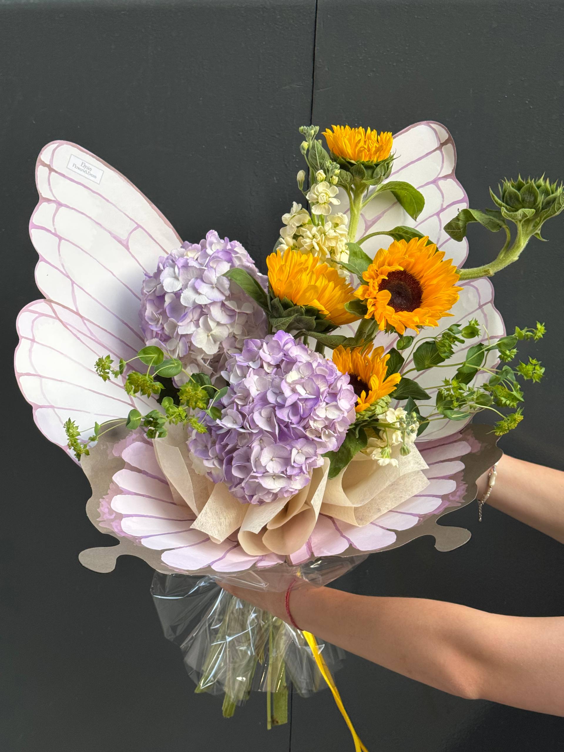 Bouquet of flowers with butterfly wings held by a person against a dark background Ramo de flores con alas de mariposa sostenidas por una persona sobre un fondo oscuro