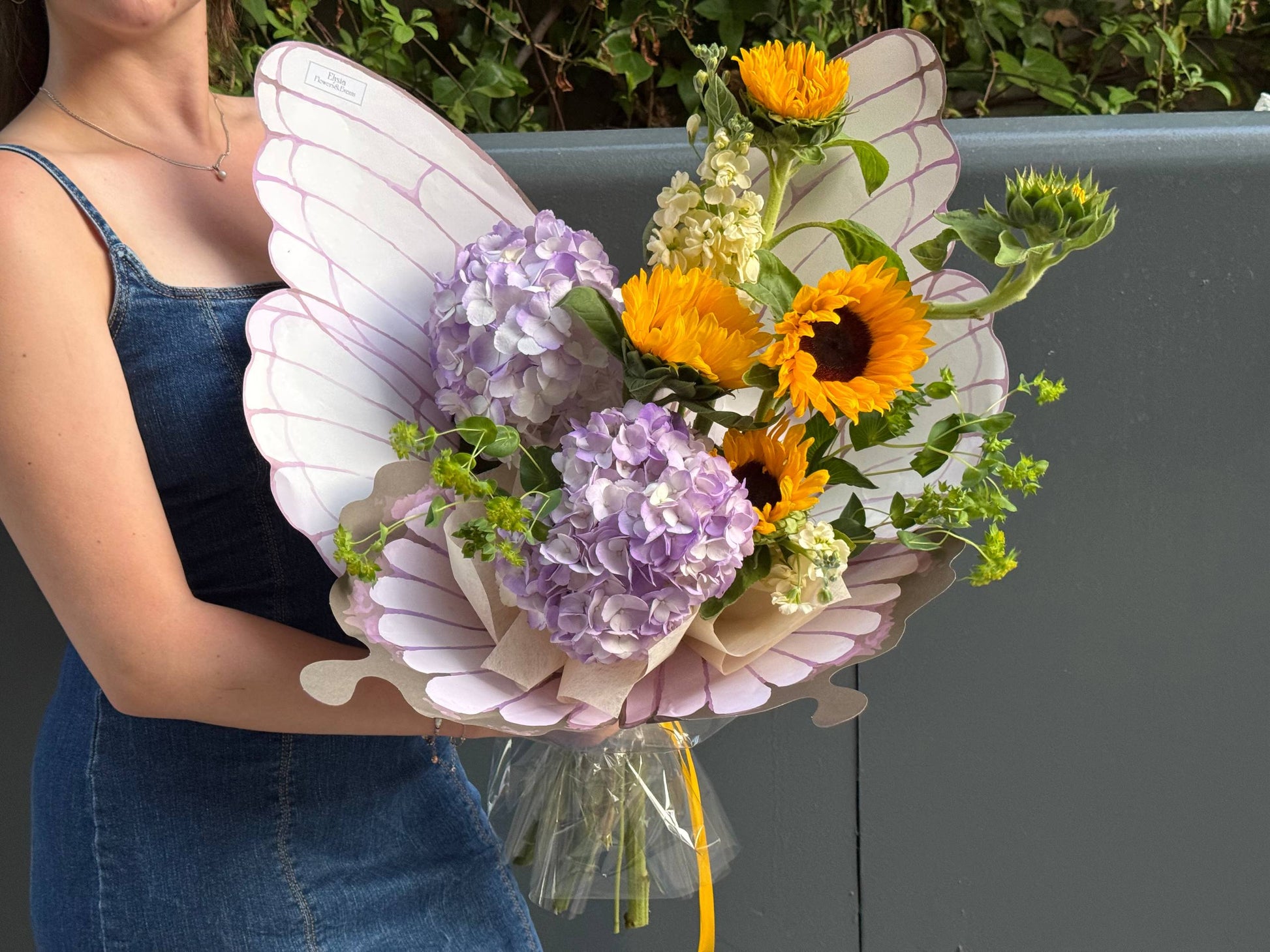 Person holding a bouquet of flowers with butterfly wings Persona sosteniendo un ramo de flores con alas de mariposa.