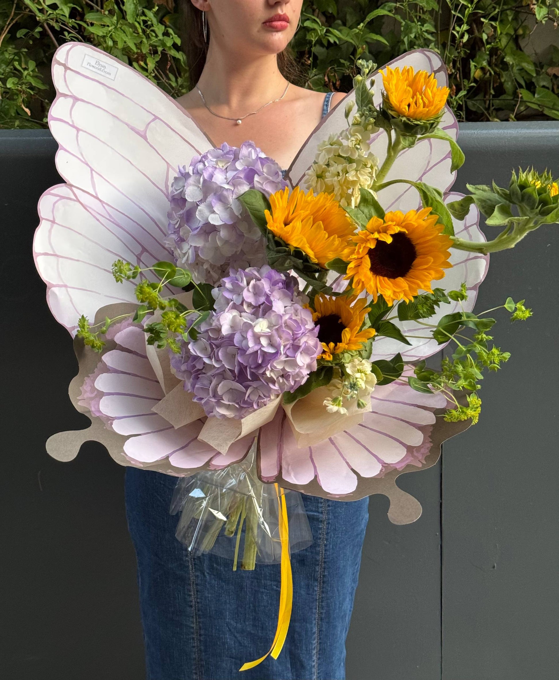 Person holding a bouquet of flowers with butterfly wings Persona sosteniendo un ramo de flores con alas de mariposa.