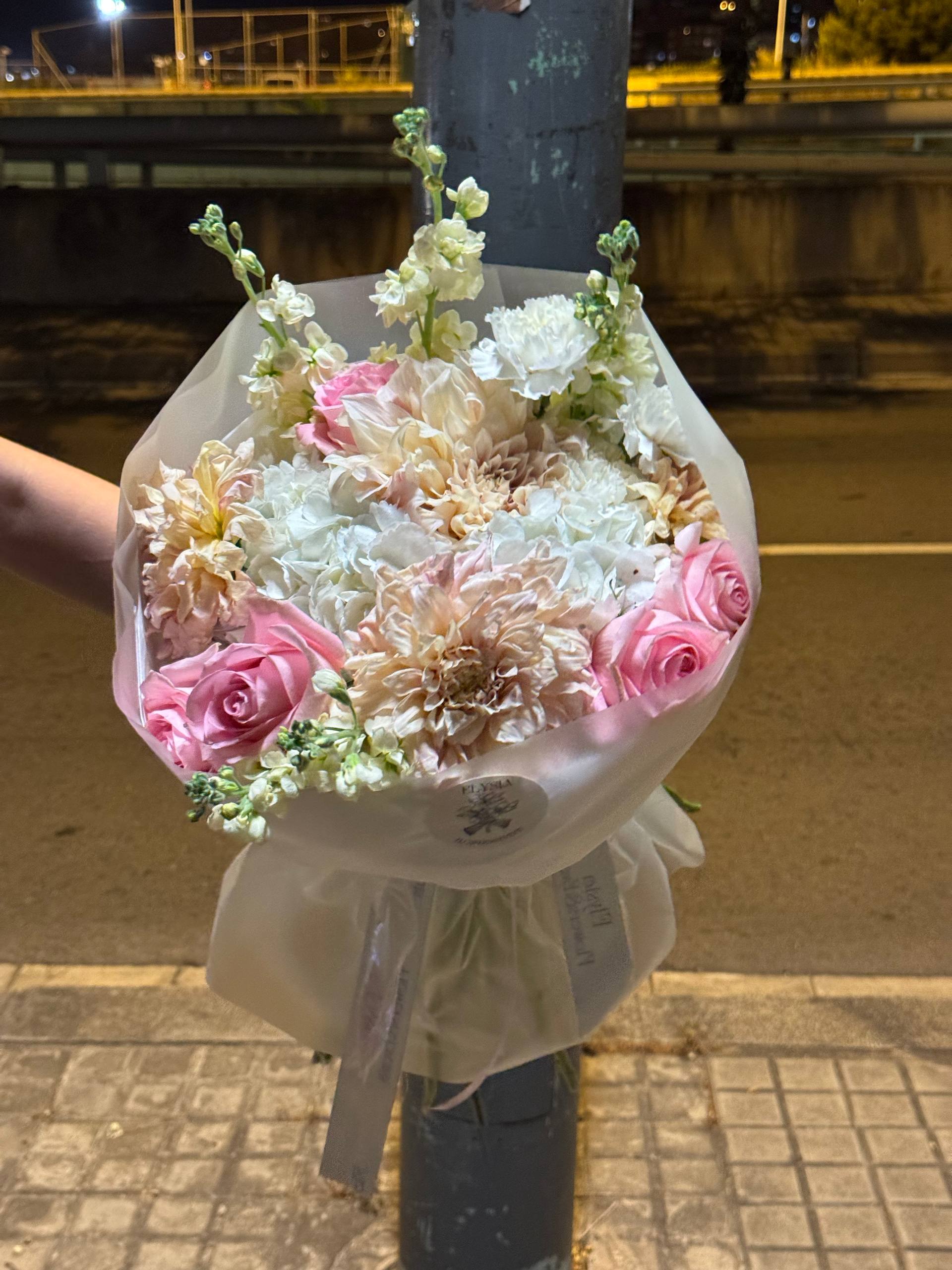 Bouquet of flowers held by a person on a street at night Ramo de flores sostenido por una persona en la calle por la noche