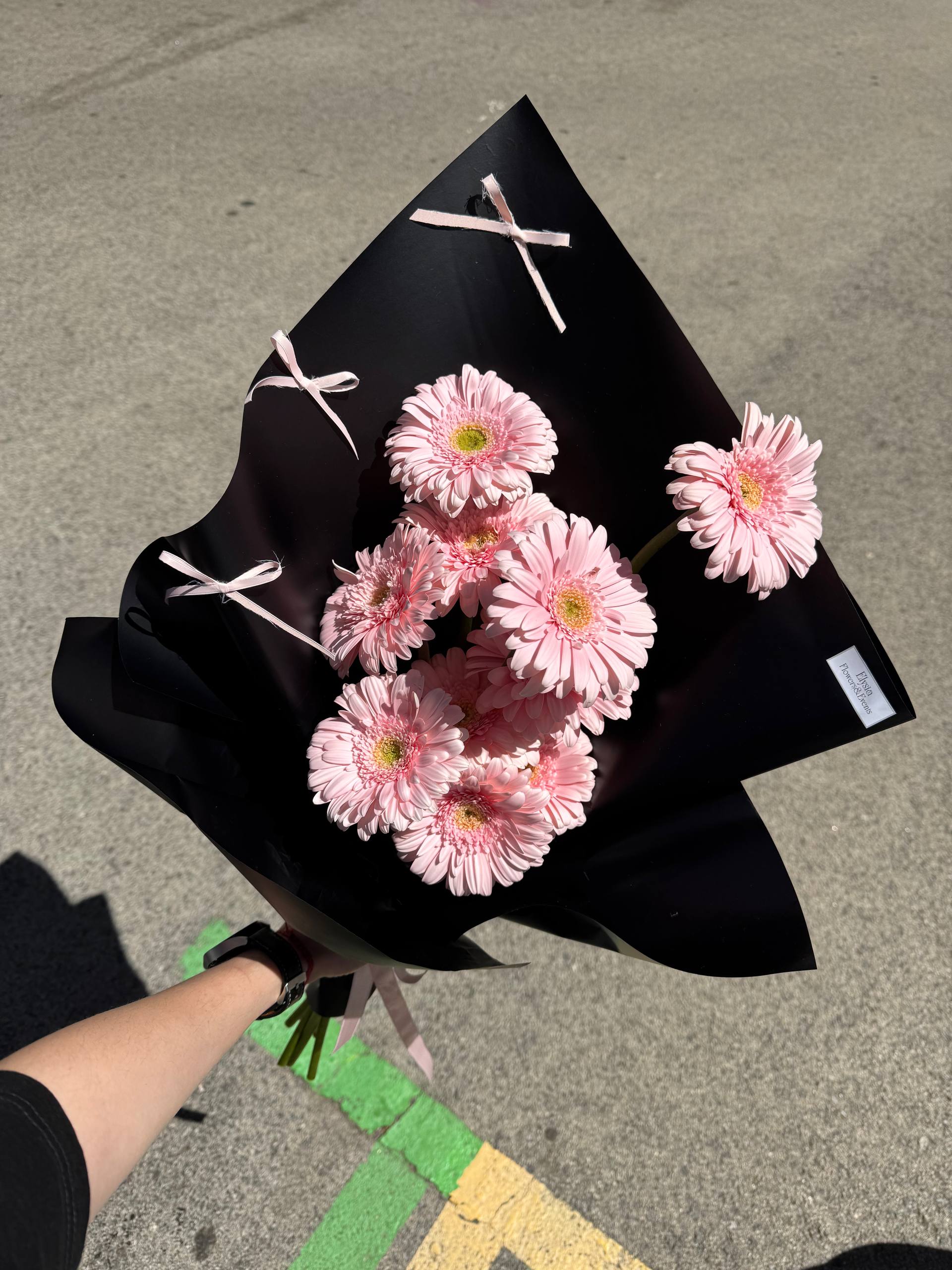 Bouquet of pink flowers wrapped in black paper with a white ribbon on a concrete surface. Bouquet of pink flowers wrapped in black paper with a white ribbon on a concrete surface.