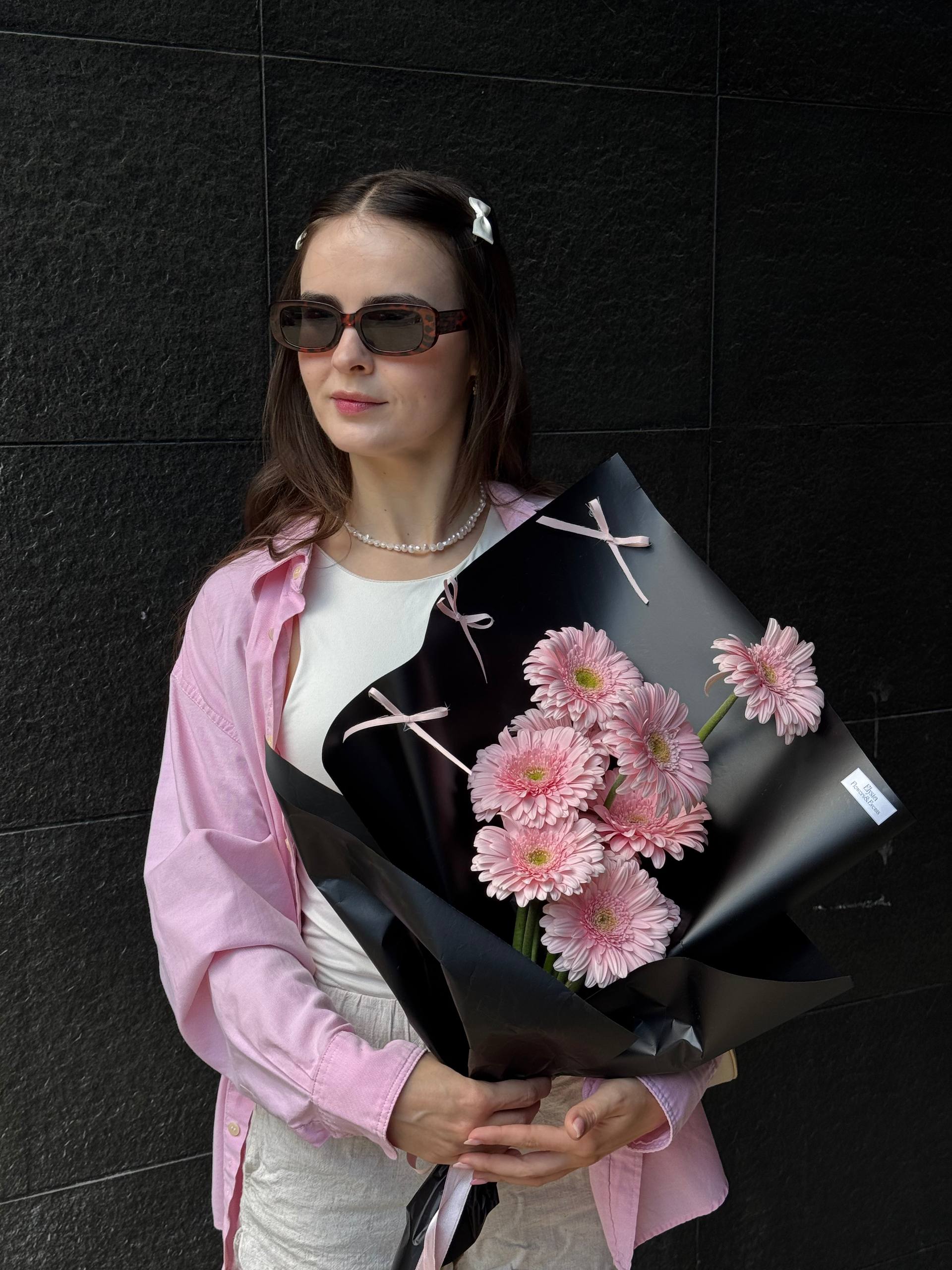 Woman holding a bouquet of pink flowers against a black wall Mujer sosteniendo un ramo de flores rosadas contra una pared negra