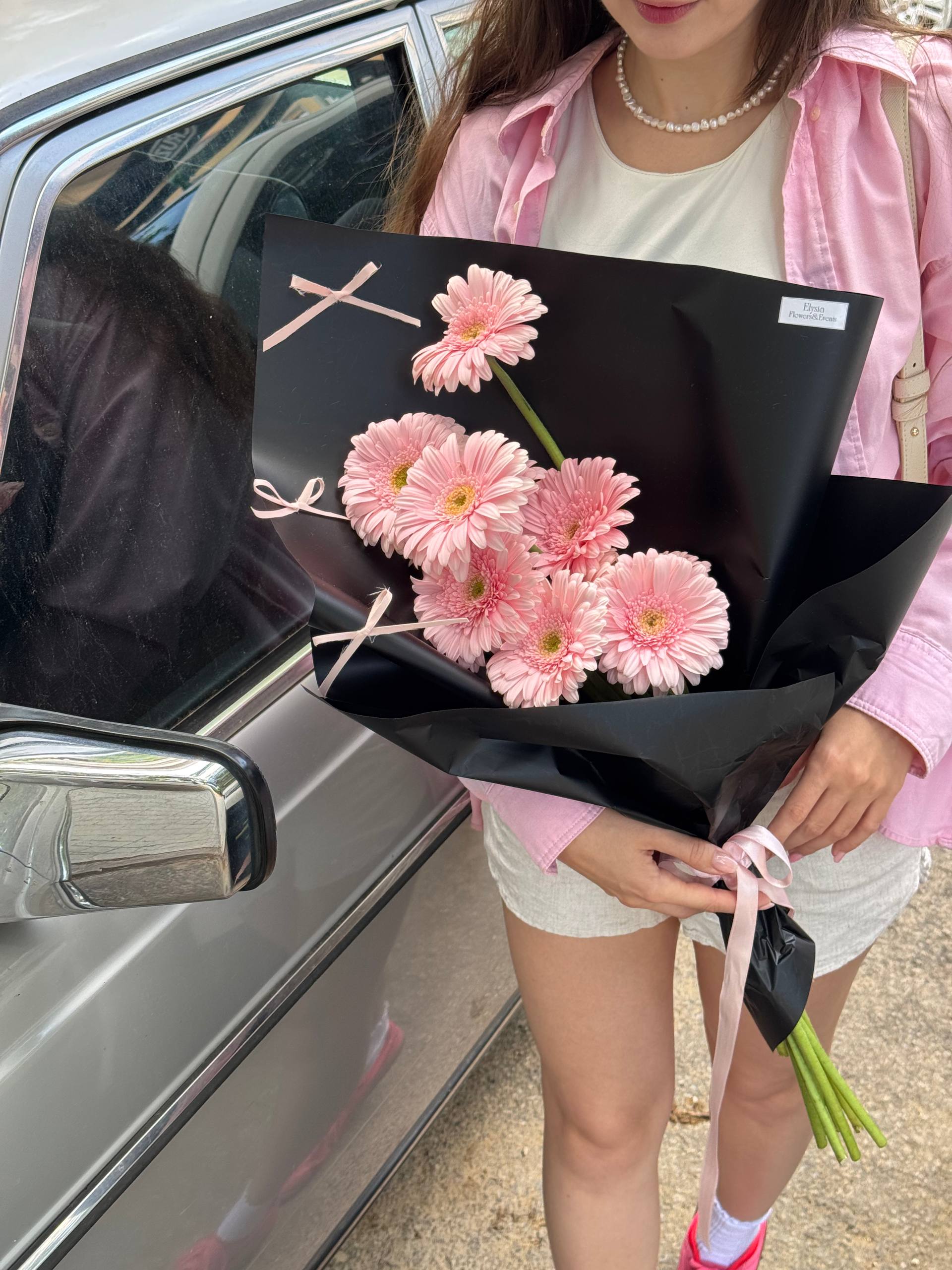 Person holding a bouquet of pink flowers in front of a car Persona sosteniendo un ramo de flores rosadas frente a un automóvil