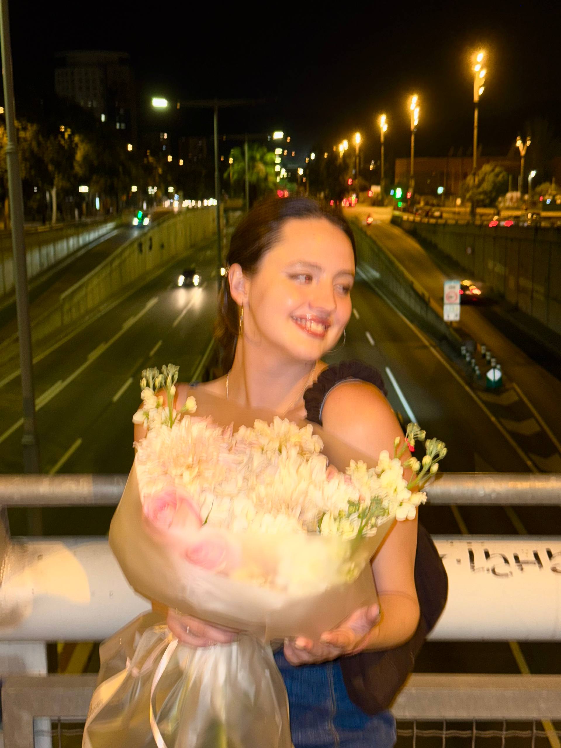 Woman holding flowers on a bridge at night with traffic in the background Woman holding flowers on a bridge at night with traffic in the background