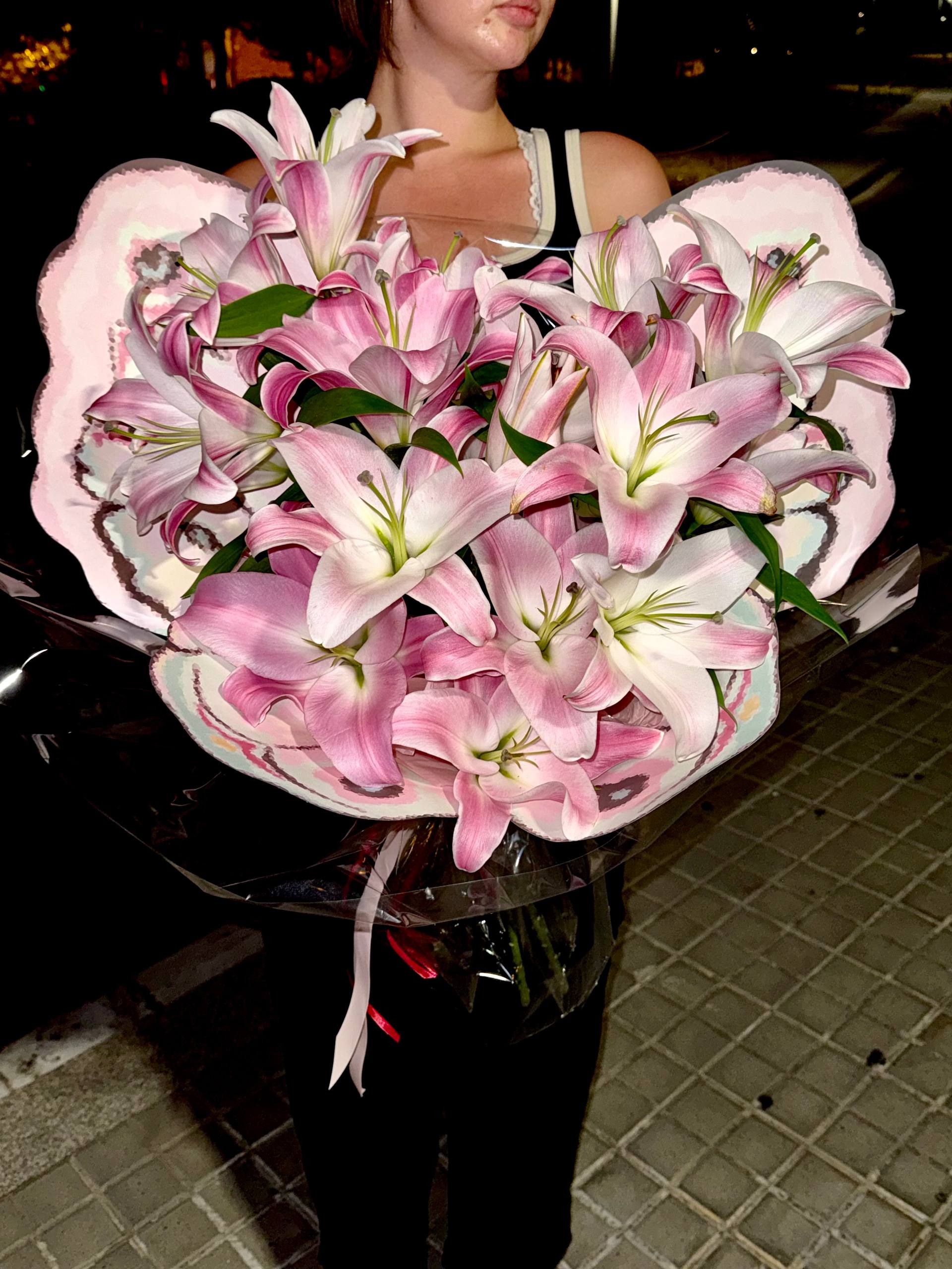 Bouquet of pink and white lilies held by a person in an urban setting. Ramo de lirios rosados y blancos sostenido por una persona en un entorno urbano.