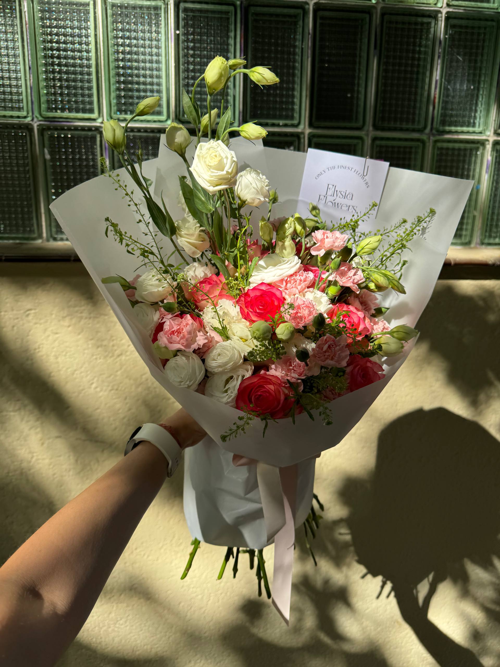 Bouquet of flowers held by a person with a glass block wall in the background Ramo de flores sostenido por una persona con una pared de bloques de vidrio al fondo