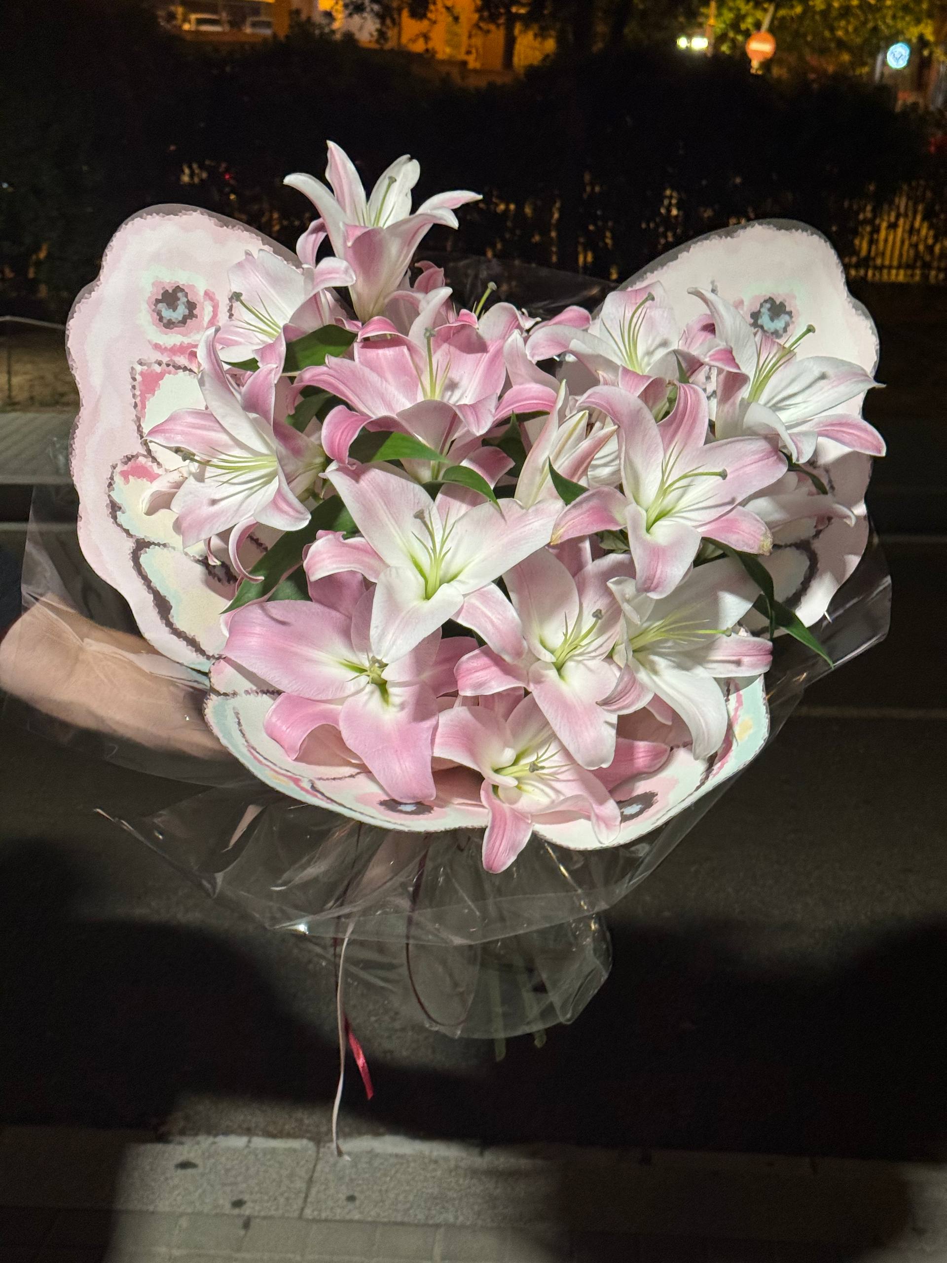 Bouquet of pink and white lilies in a clear plastic wrap against a dark background. Ramo de lirios rosados y blancos en una envoltura de plástico transparente sobre un fondo oscuro.