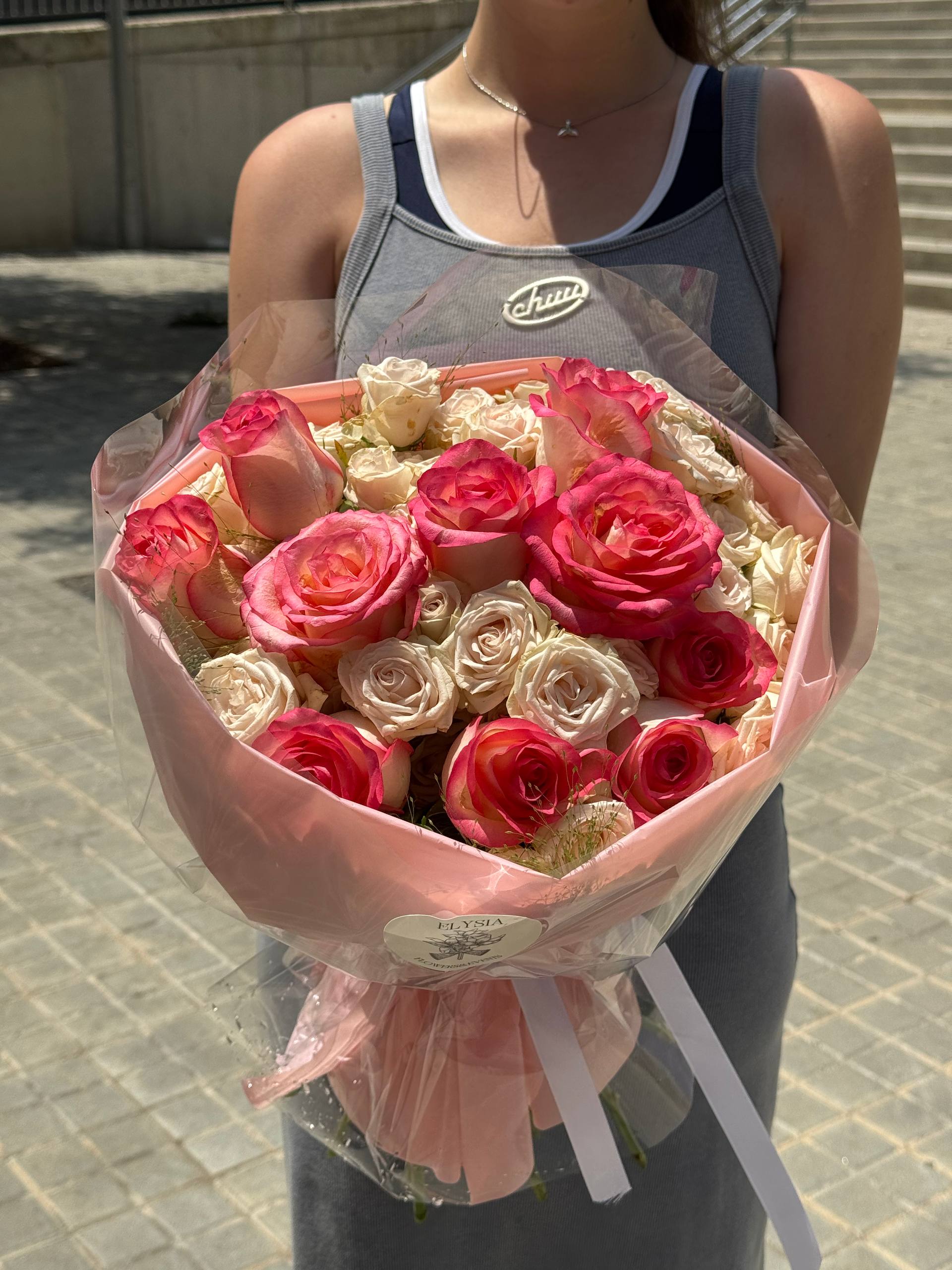 Person holding a bouquet of pink and white roses outdoors. Persona sosteniendo un ramo de rosas rosadas y blancas al aire libre.