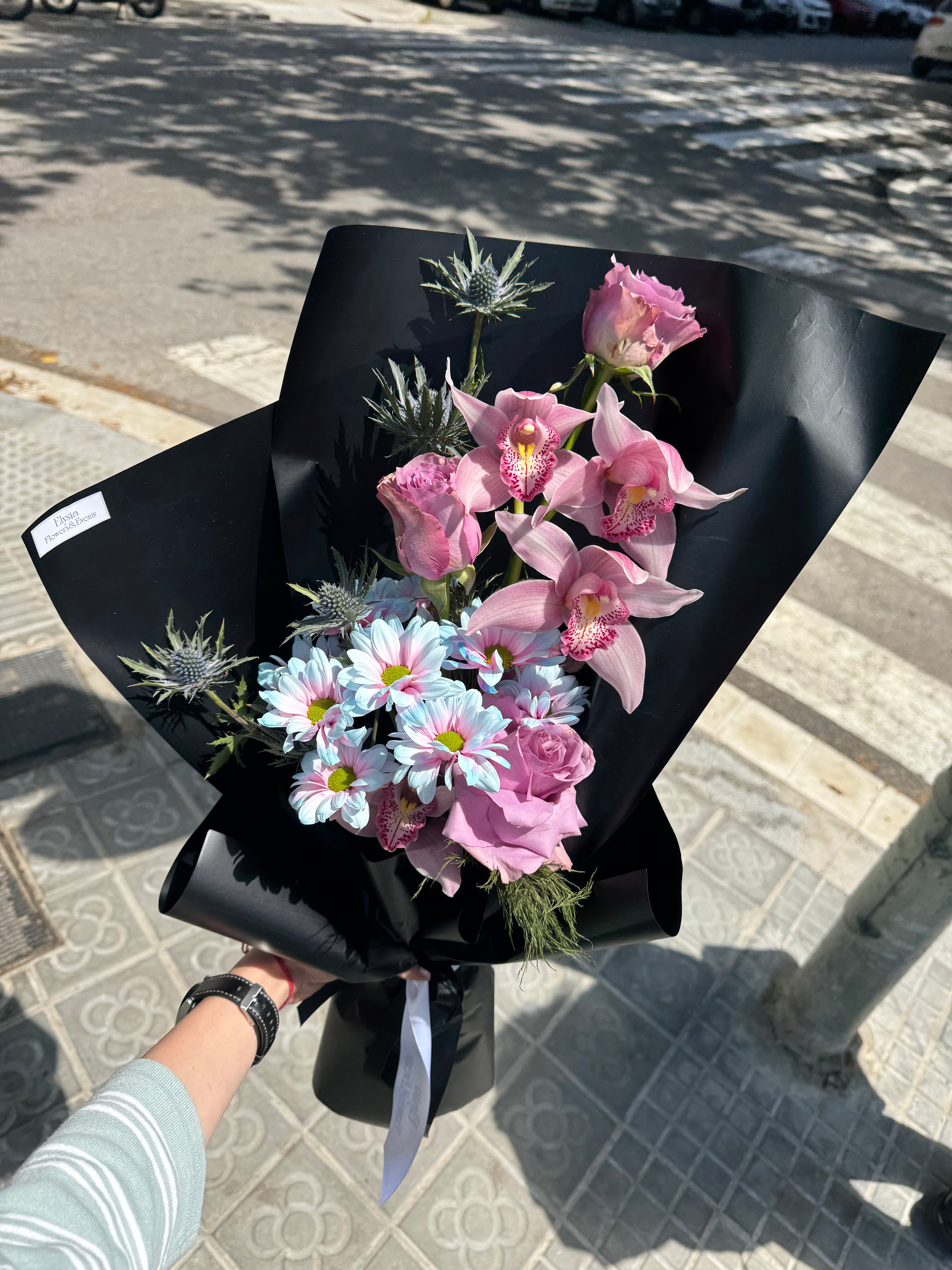 Bouquet of flowers wrapped in black paper held by a person on a street. Ramo de flores envuelto en papel negro sostenido por una persona en una calle.