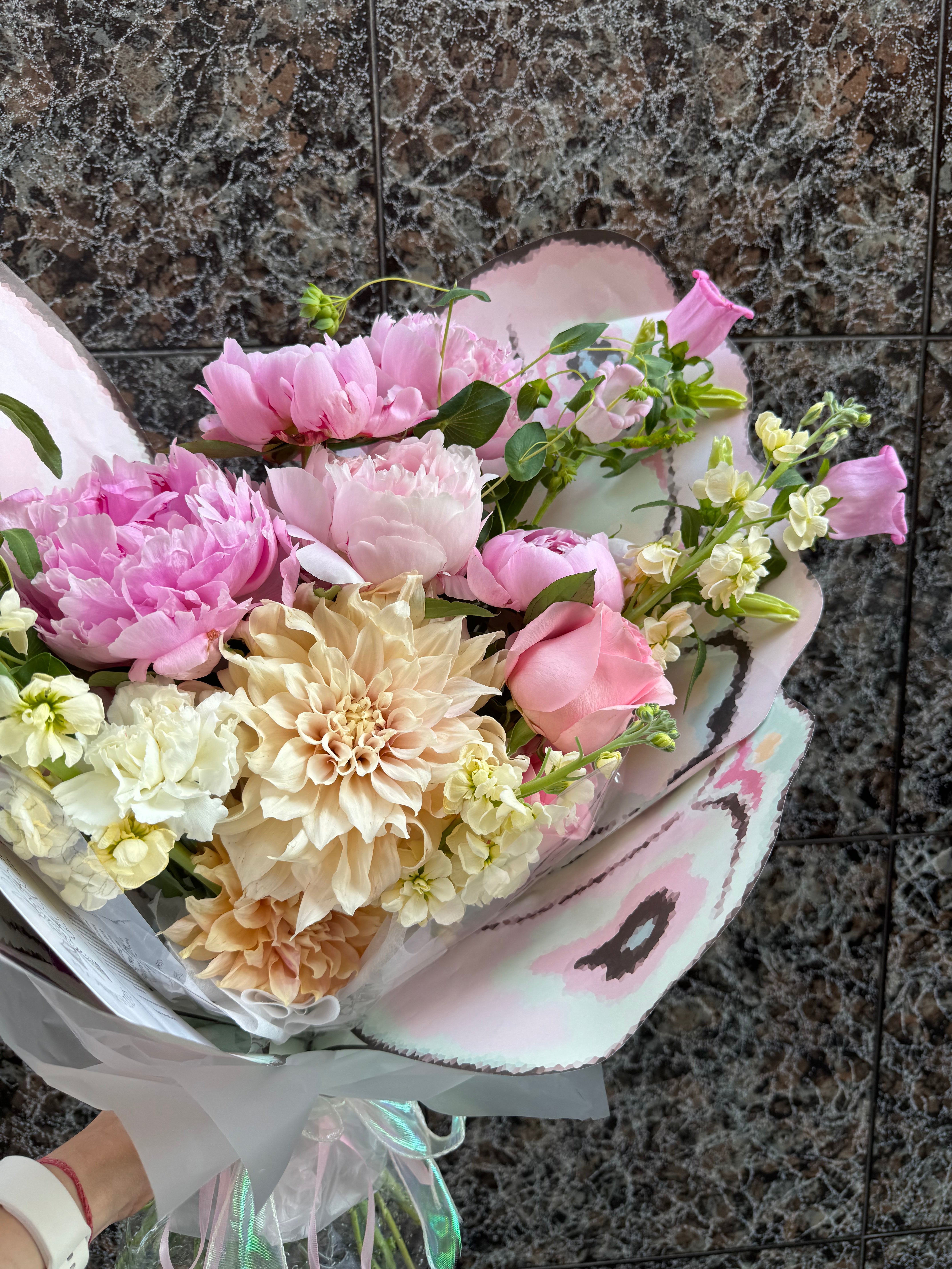 Bouquet of pink, white, and beige flowers held against a tiled wall. Ramo de flores rosas, blancas y beige contra una pared de azulejos.