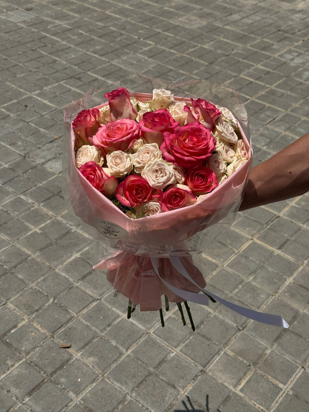 Bouquet of pink and white roses held by a person on a paved ground. Ramo de rosas rosadas y blancas sostenido por una persona en un suelo pavimentado.