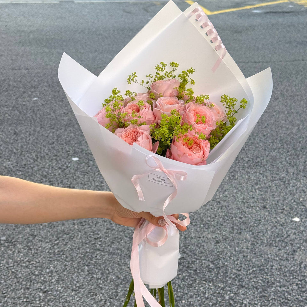 Bouquet of pink flowers wrapped in white paper with a pink ribbon held by a person on a gray pavement. Bouquet of pink flowers wrapped in white paper with a pink ribbon held by a person on a gray pavement.