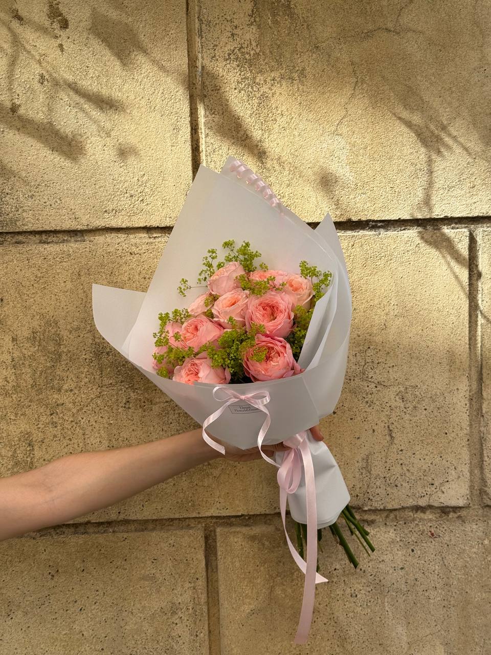 Bouquet of pink roses held against a stone wall Ramo de rosas rosadas sostenido contra un muro de piedra