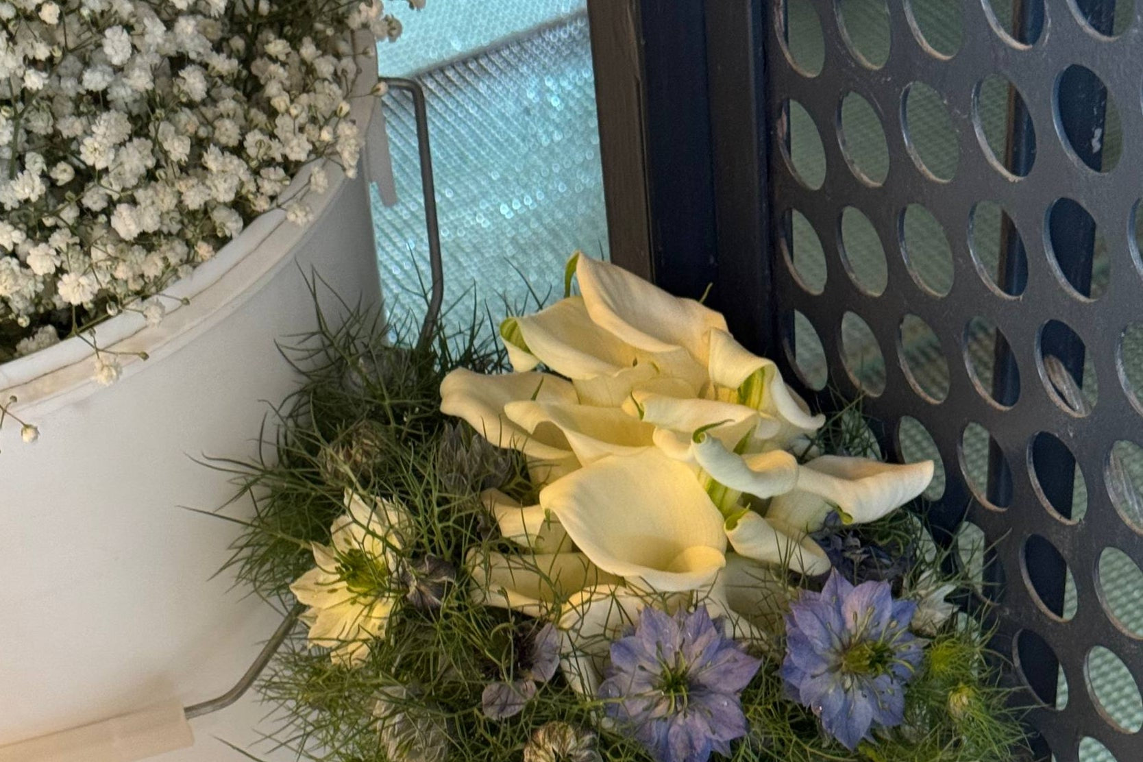 Decorative bridal arrangement of white flowers and greenery with a metal grid background Arreglo nupcial decorativo de flores blancas y vegetación con fondo de rejilla metálica