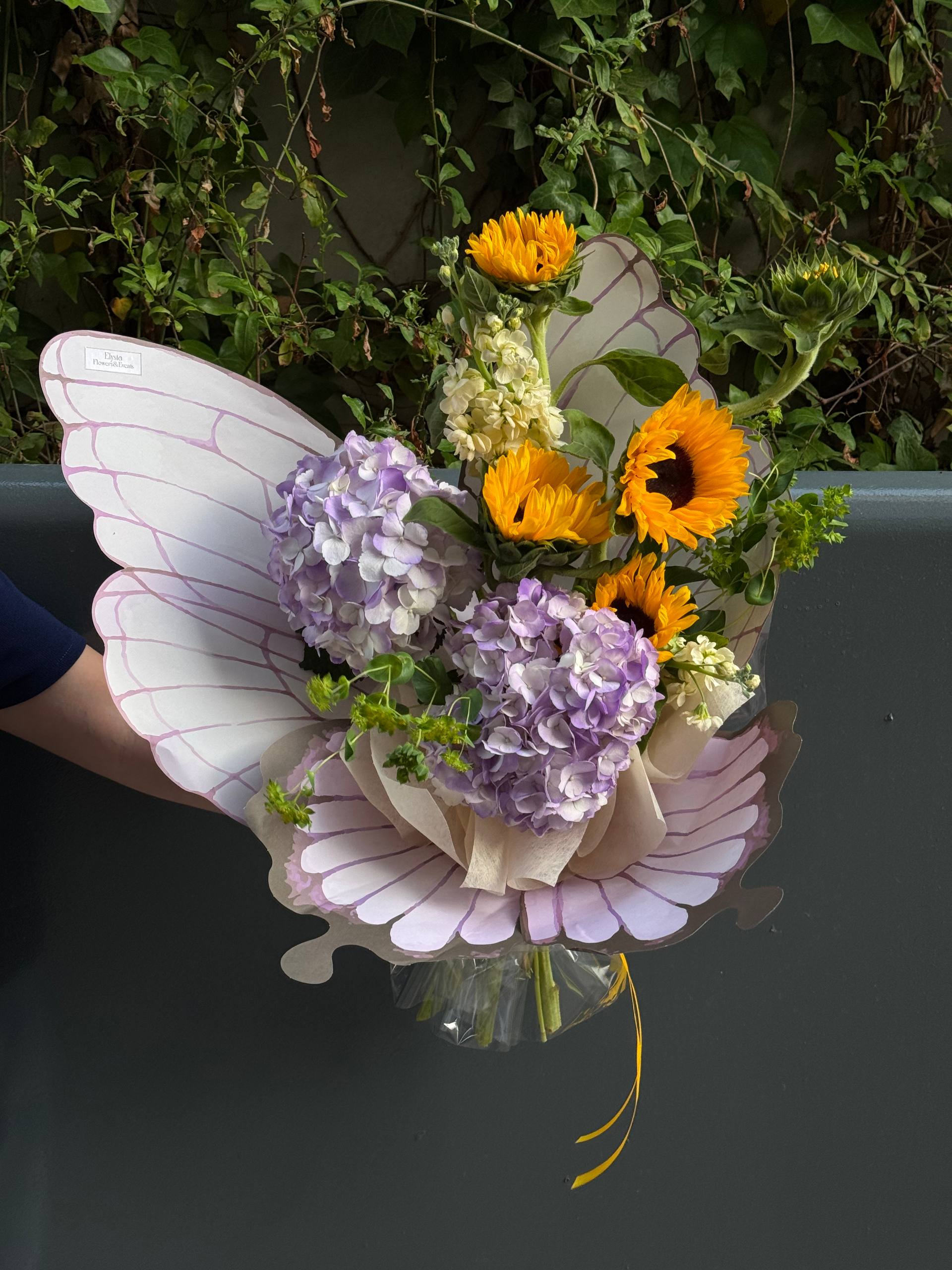 Floral arrangement with butterfly wings against a green leafy background Arreglo floral con alas de mariposa sobre un fondo verde frondoso
