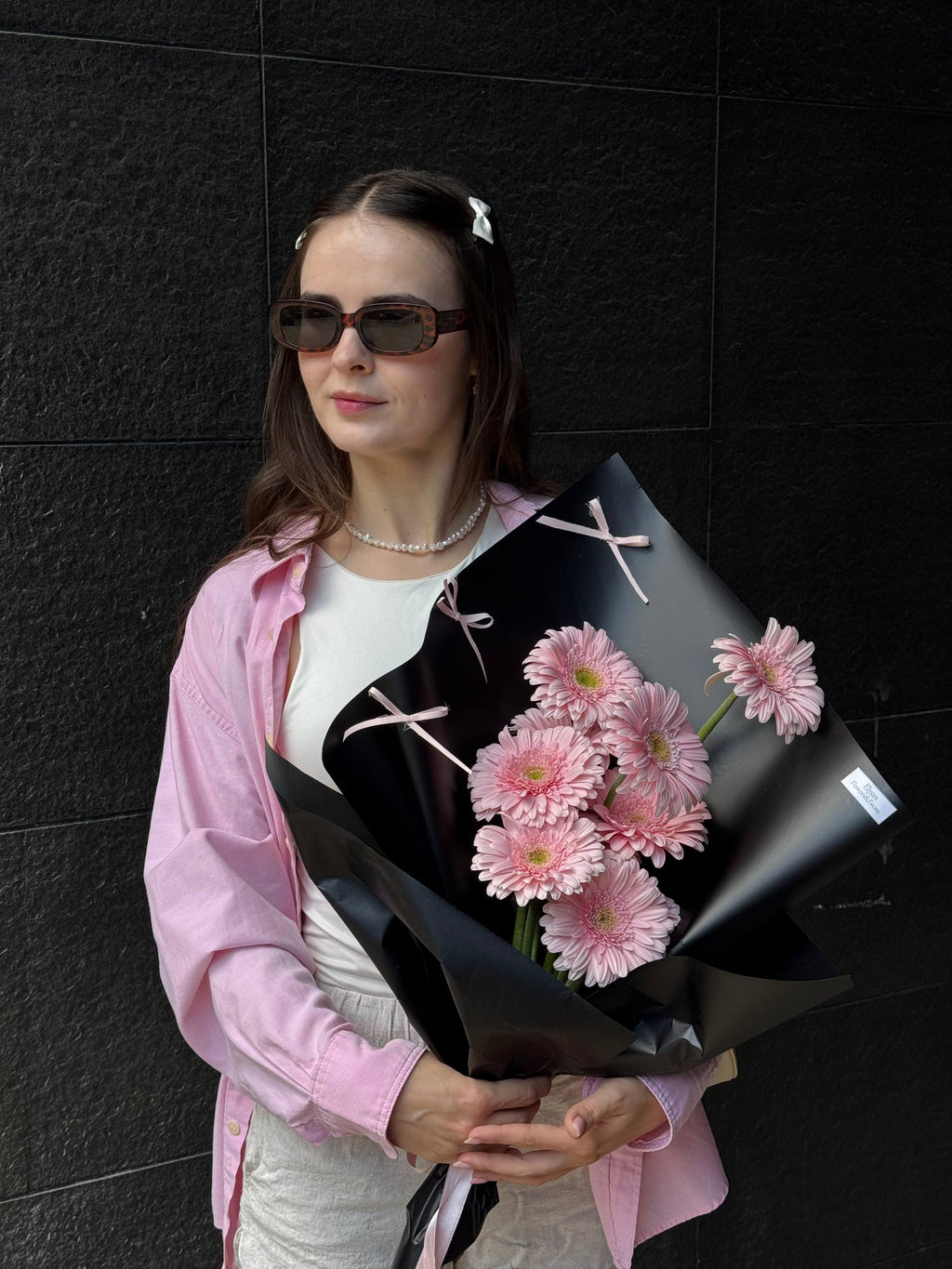Woman holding a bouquet of pink flowers against a black wall Mujer sosteniendo un ramo de flores rosadas contra una pared negra