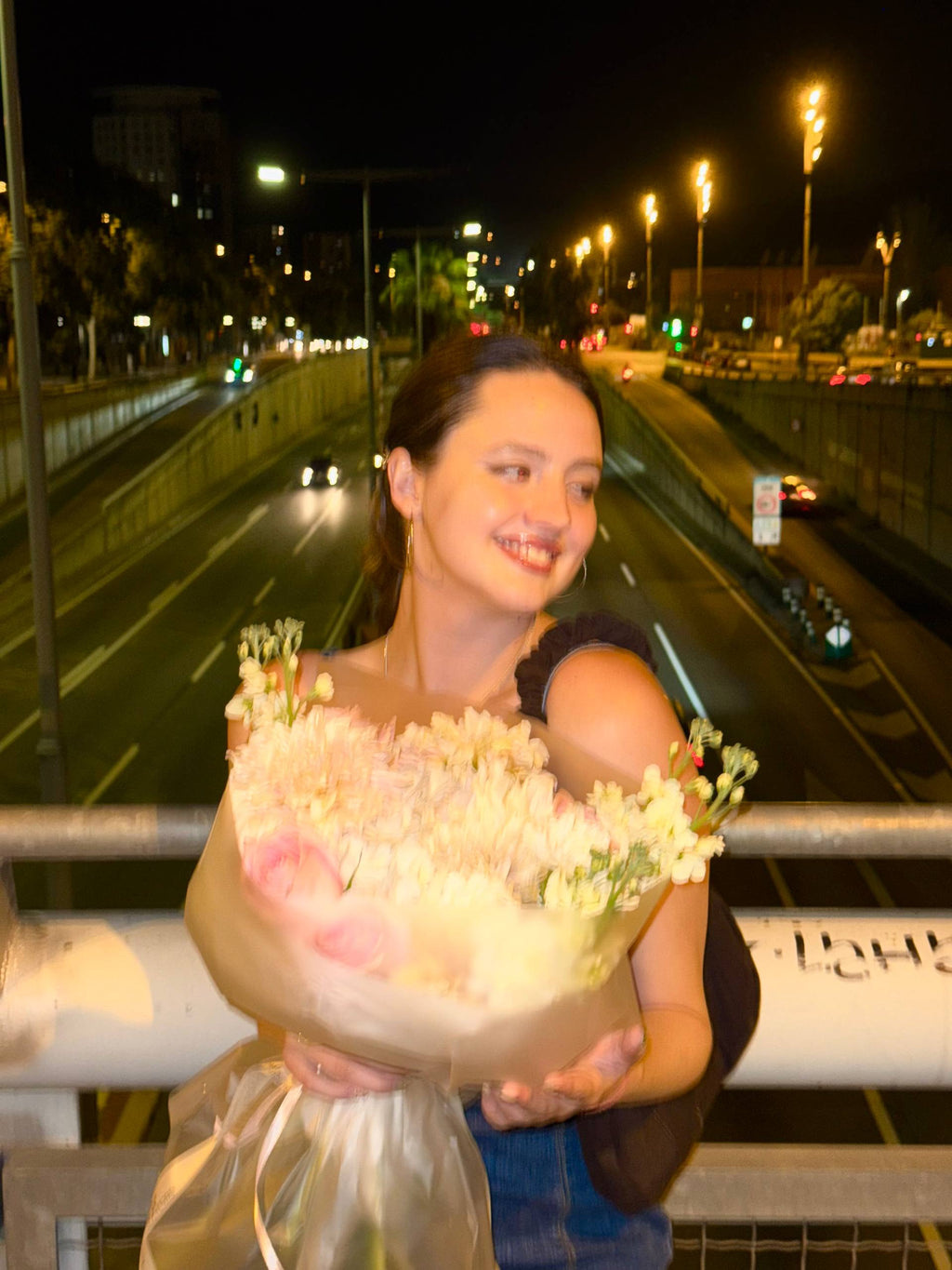 Woman holding flowers on a bridge at night with traffic in the background Woman holding flowers on a bridge at night with traffic in the background