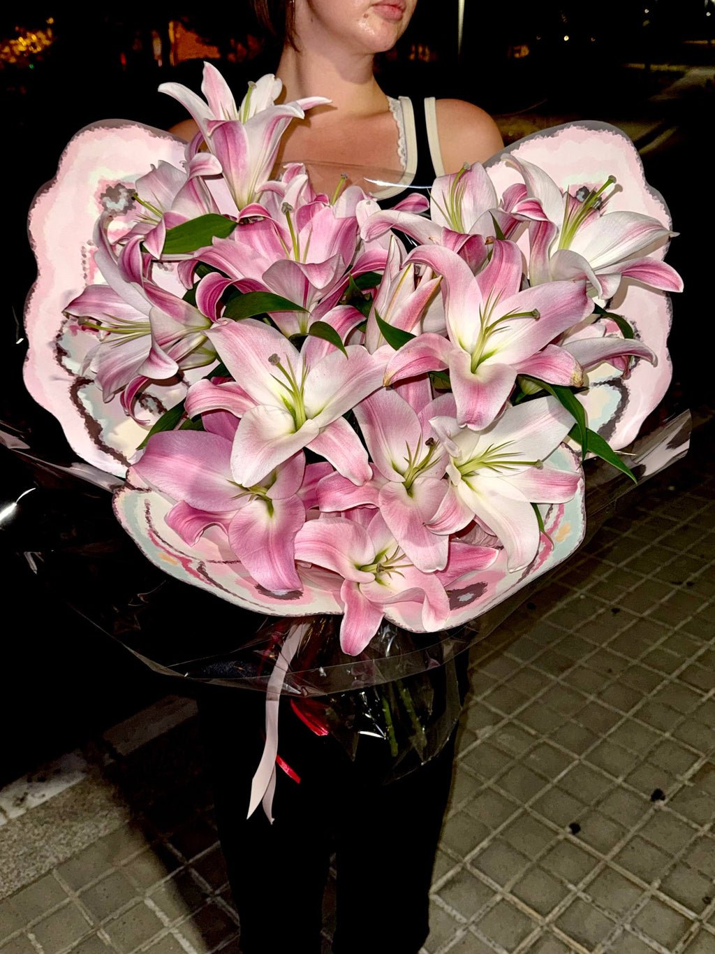 Bouquet of pink and white lilies held by a person in an urban setting. Ramo de lirios rosados y blancos sostenido por una persona en un entorno urbano.