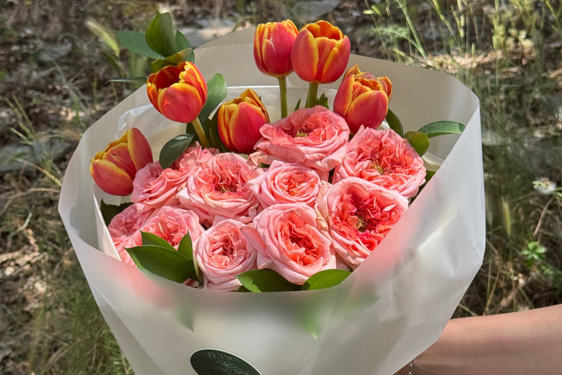 Bouquet of pink flowers and tulips held outdoors with a natural background  Ramo de flores rosadas y tulipanes al aire libre con un fondo natural